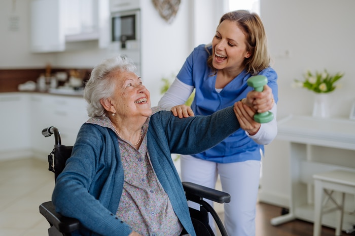 Nurse exercising with senior woman at her home, concept of healthcare and rehabilitation.